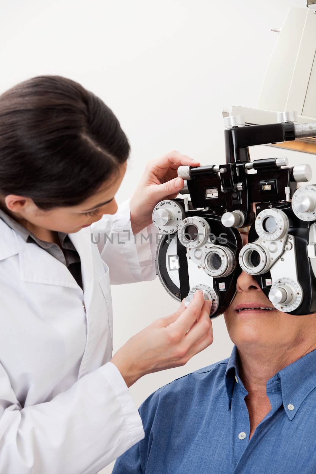 Female optometrist adjusting panels of phoropter during eye checkup