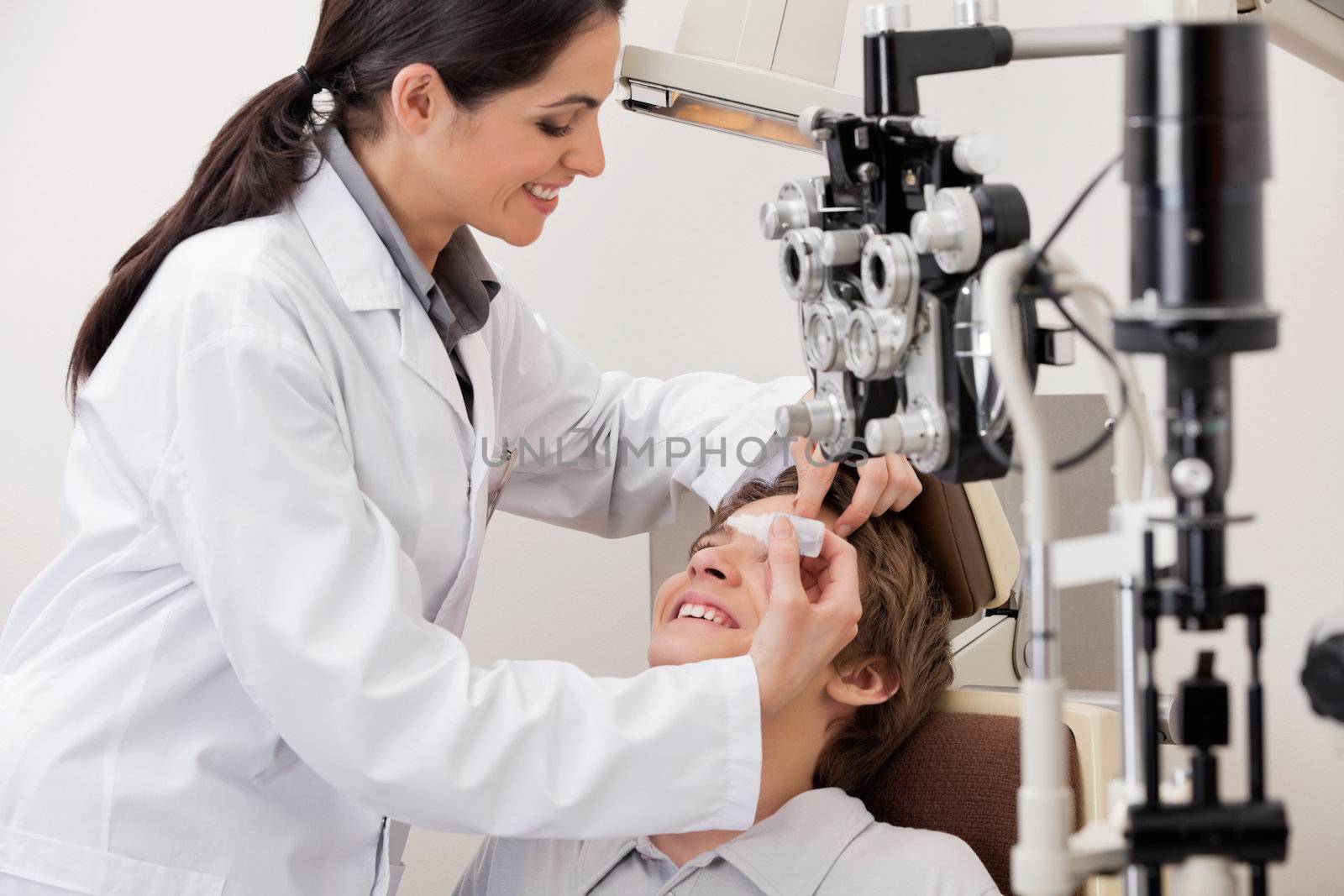 Smiling young optometrist putting eye drops in eyes of patient for clear vision