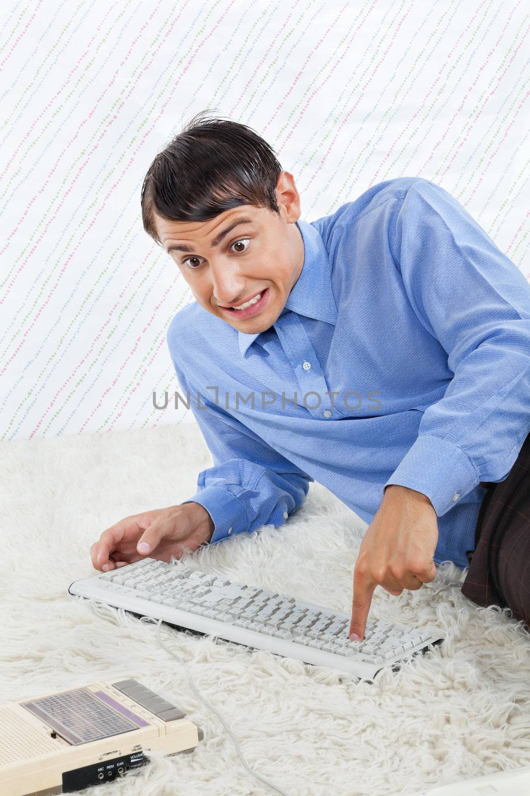 Geek businessman lying on rug with computer keyboard and vintage cassette player