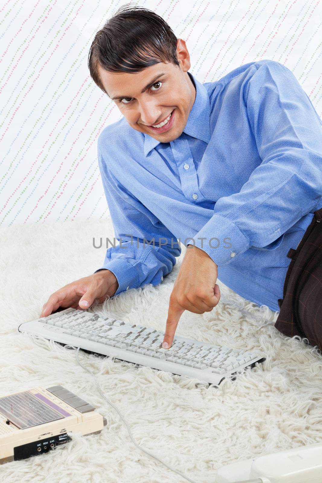 Portrait of geek businessman pressing keyboard keys while lying down on rug with an old fashioned cassette player