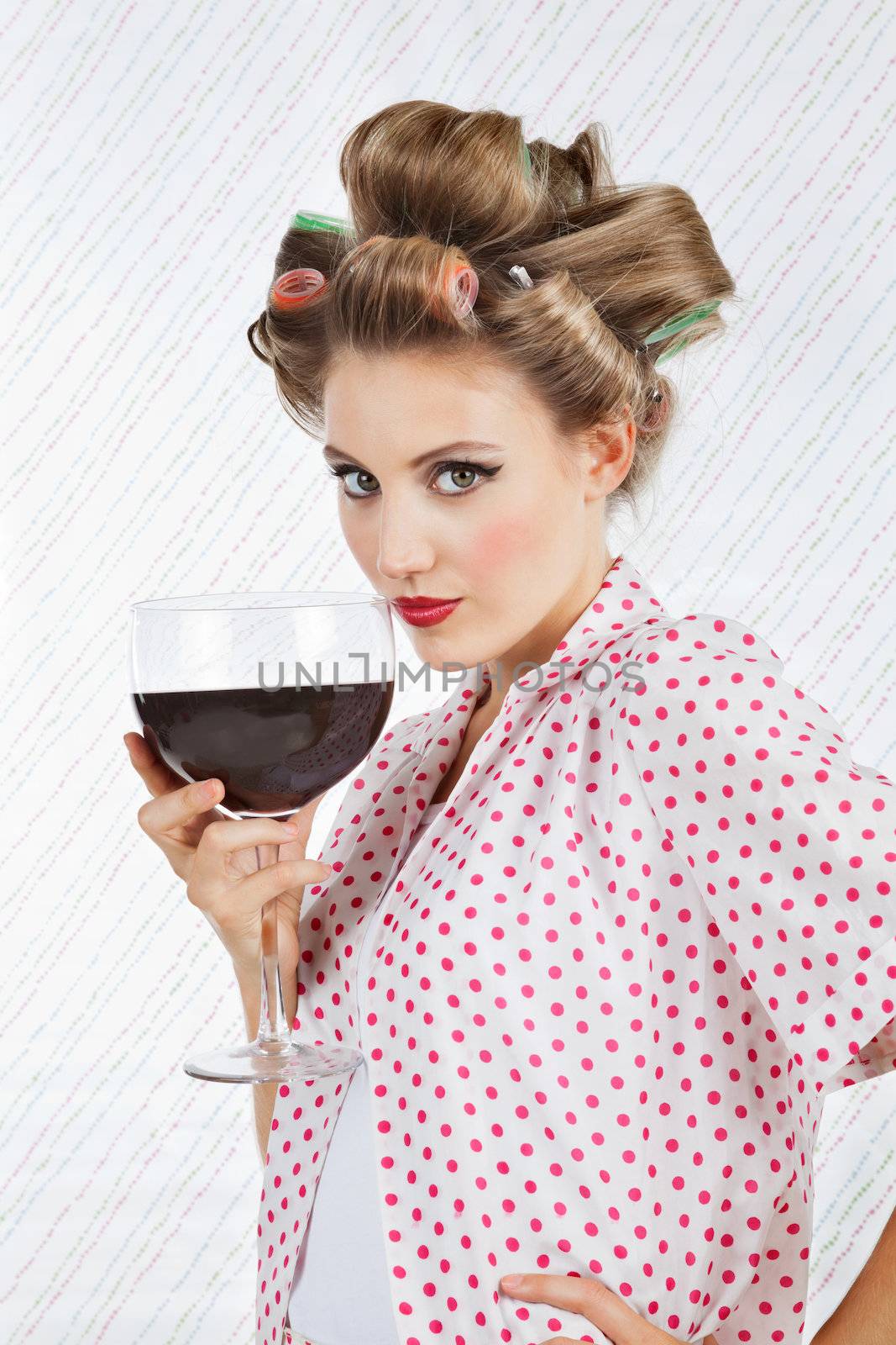 Portrait of beautiful young female with hair curlers holding giant glass of wine