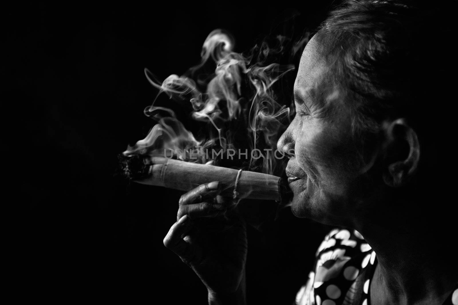 Old wrinkled Asian woman smoking traditional tobacco in monotone, black and white portrait. Bagan, Myanmar.