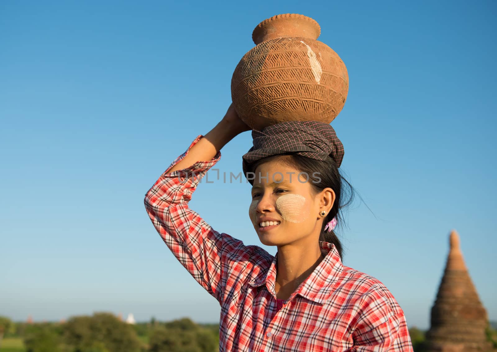 Portrait of Asian traditional female farmer carrying clay pot on head going back home, Bagan, Myanmar 