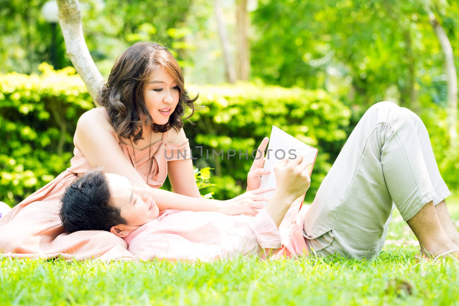 Couple relaxing in the garden, young man reading a book and resting on his girlfriend lap