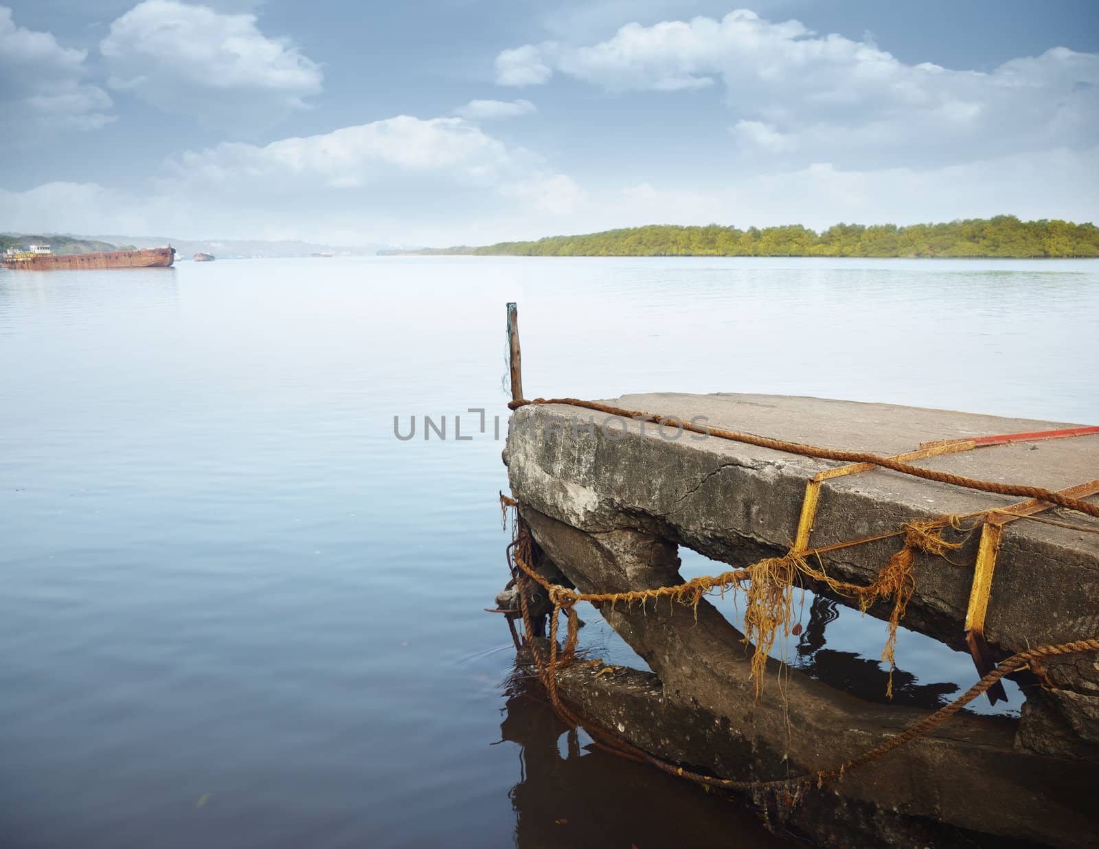 Old stony jetty with ropes and old barge in the background