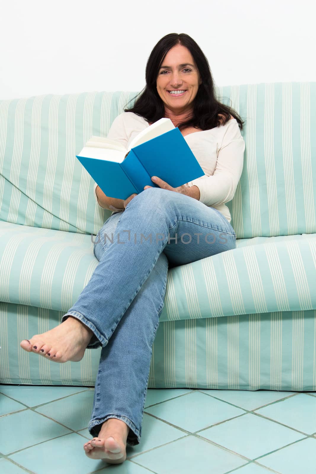Dark haired woman lying on couch and reading a blue book
