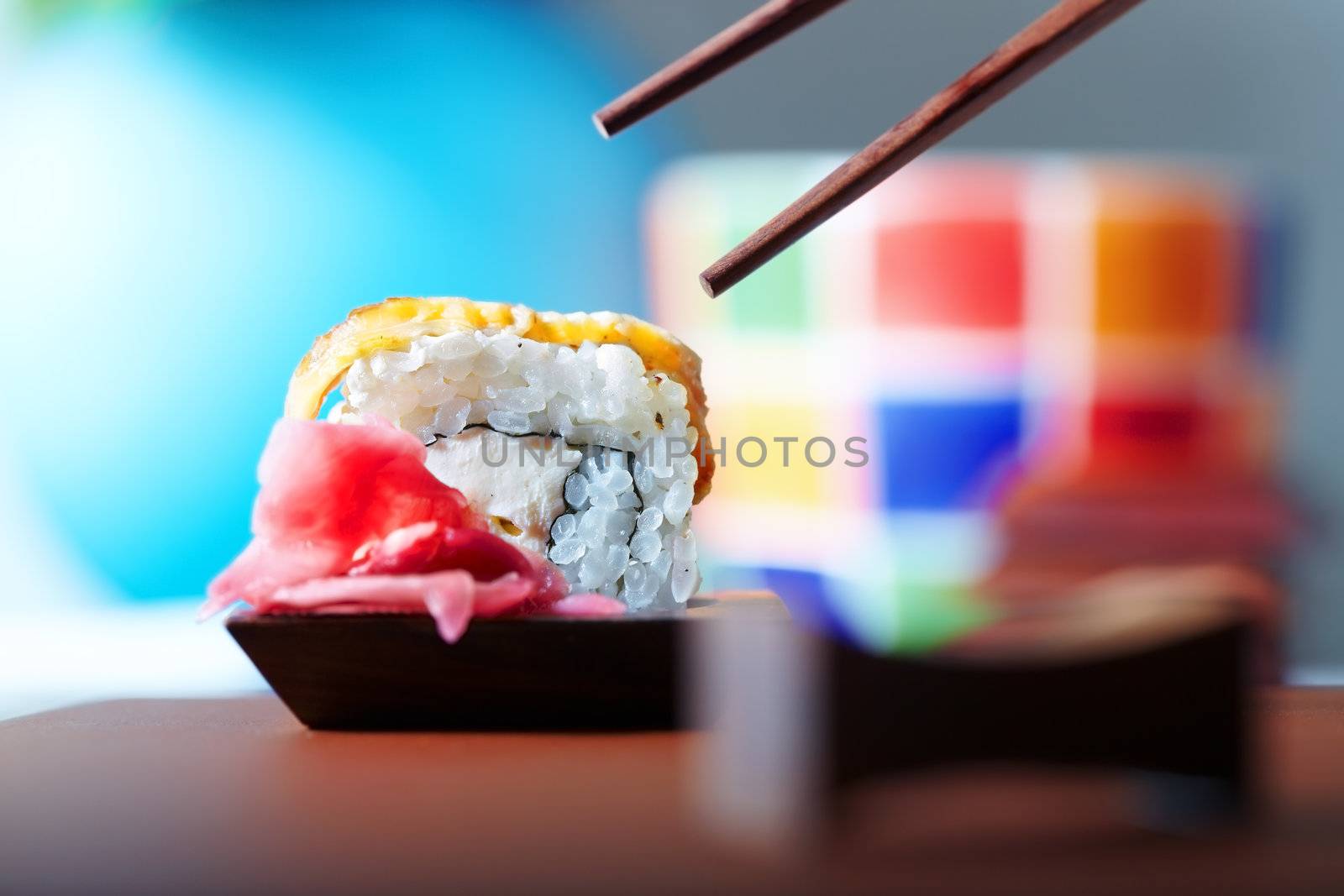 Close-up horizontal photo of the rolled sushi with ginger on the table and chopsticks
