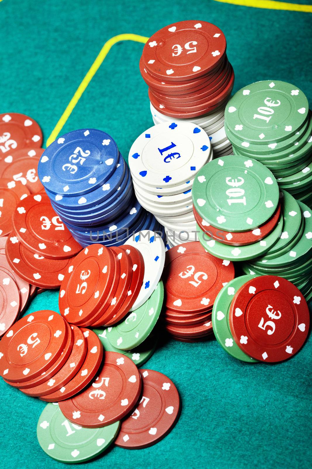 Vertical close-up photo of the various casino chips on a green table