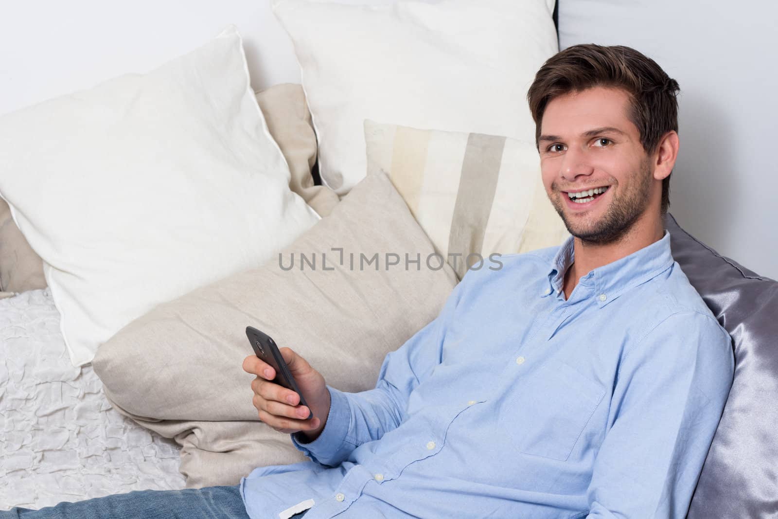 Young brunette man in blue shirt using cellphone on couch