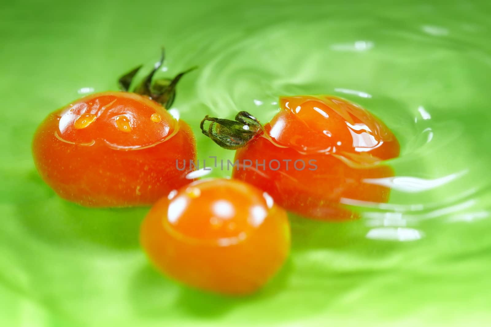 Three small tomatos in water on a green background.  Close-up photo