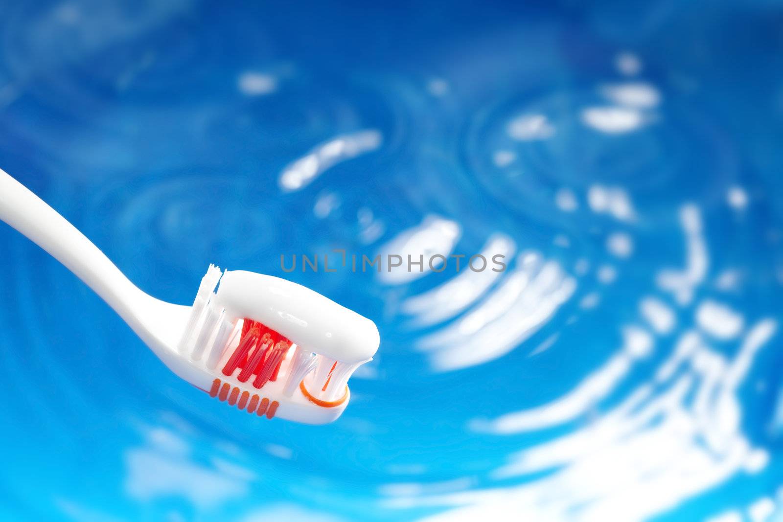 Close-up photo of the toothbrush with paste on a blue water background. Natural colors