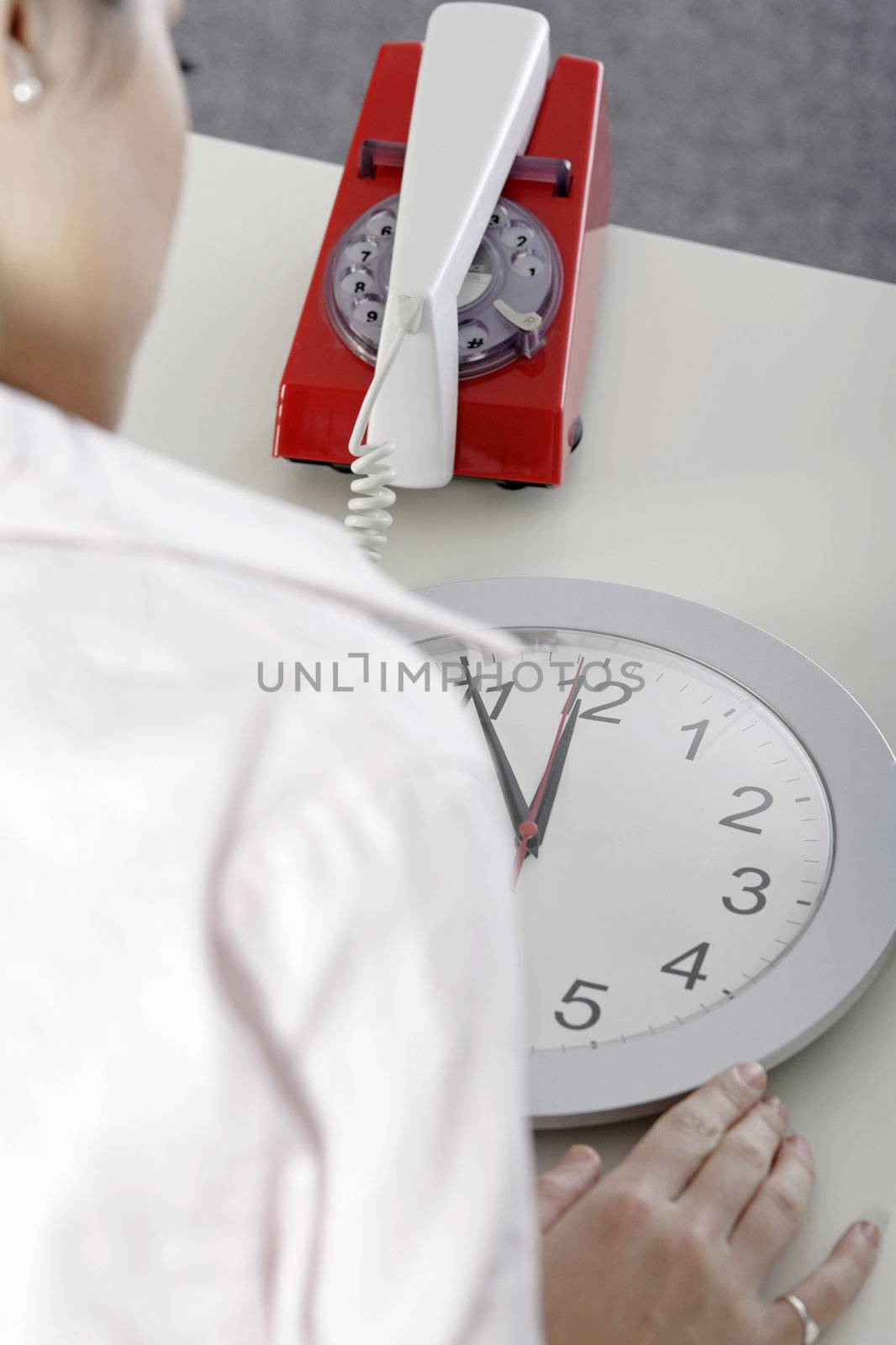 Woman watching the minutes pass on a clock at her desk waiting.