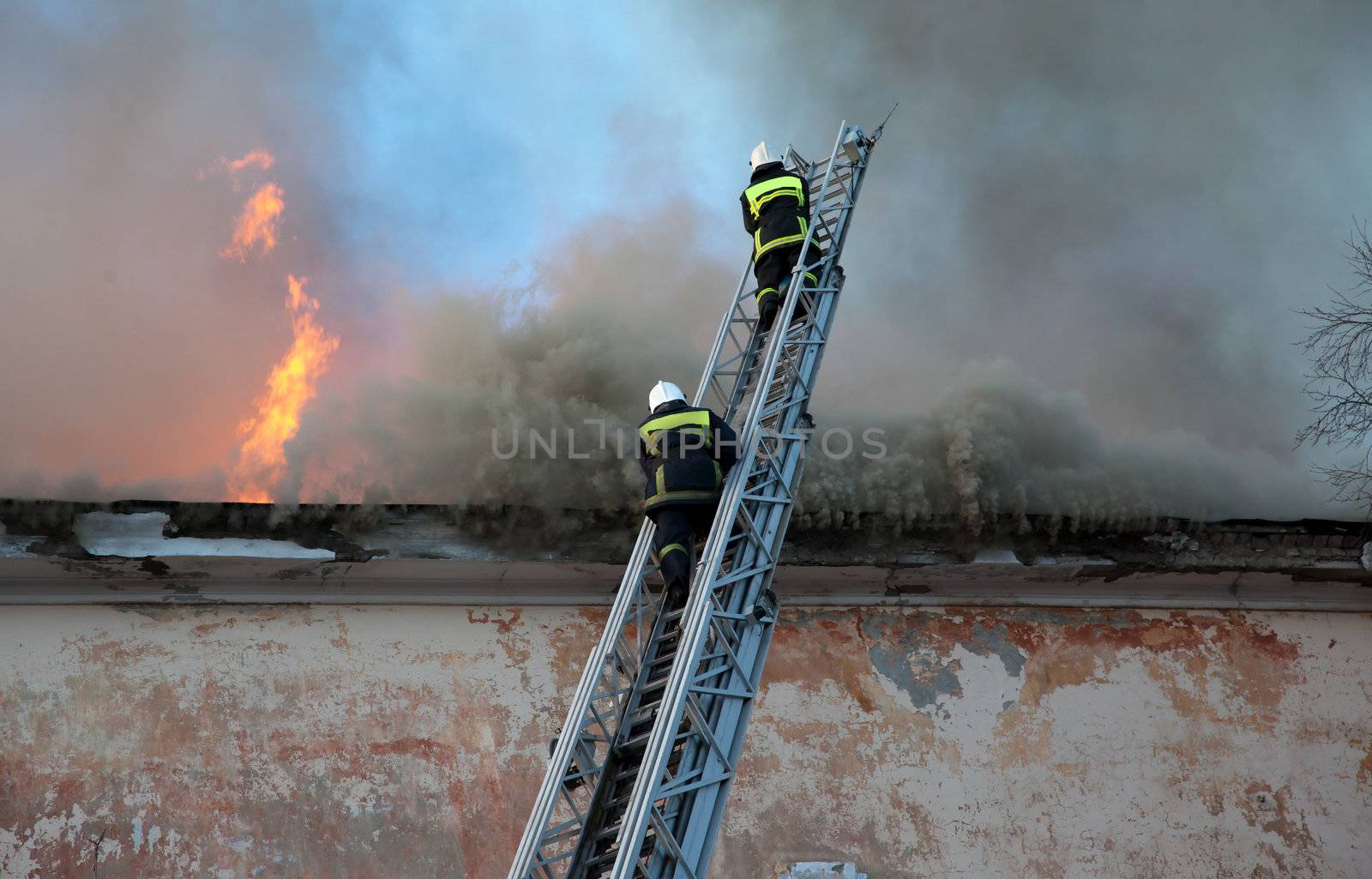 Firefighters extinguish fire from a high ladder against the background of a burning building roof