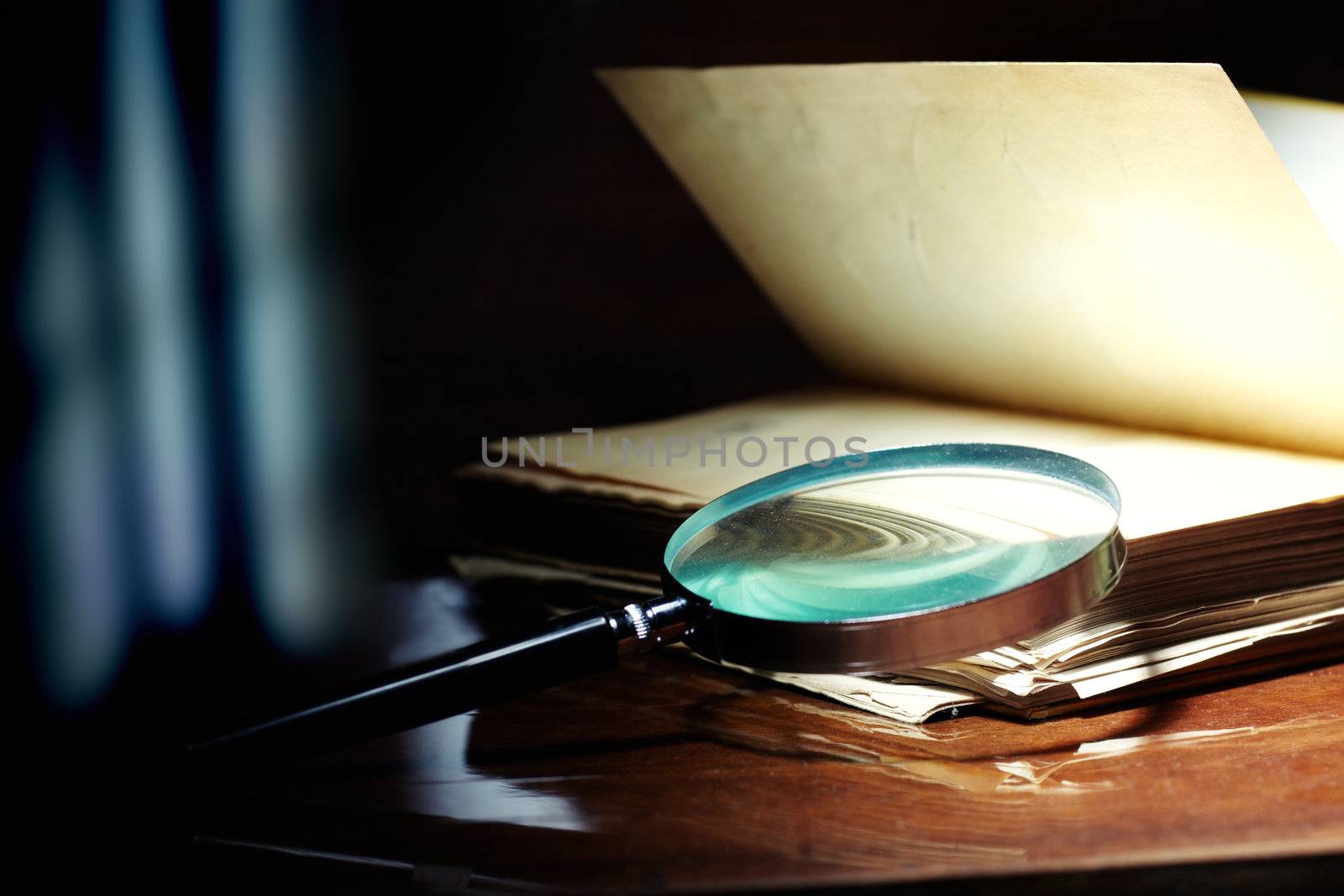 Old book and magnifier glass on a dark background as a symbol of knowledge and science