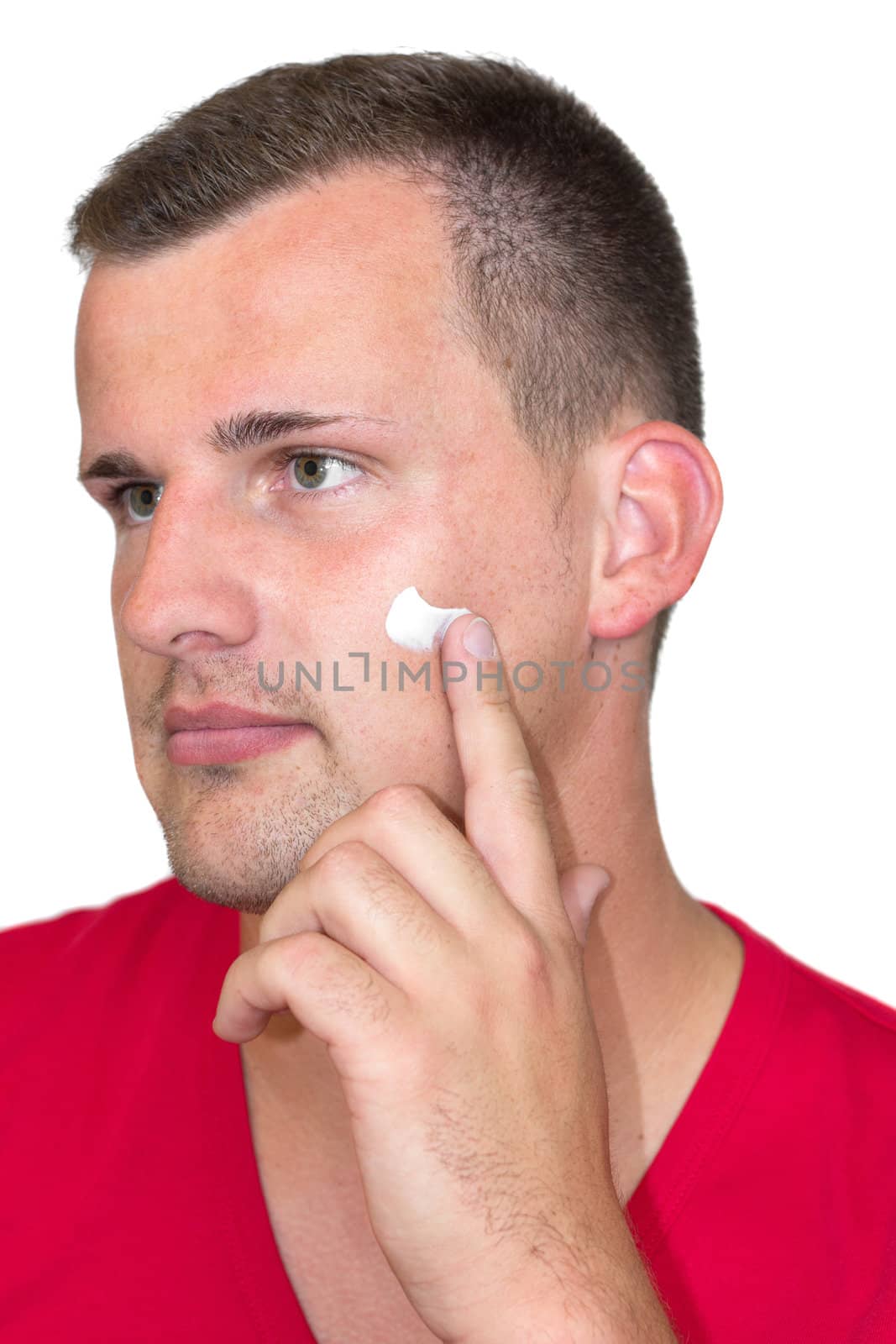 Young white man with moisturizer cream in his face in front of isolated background