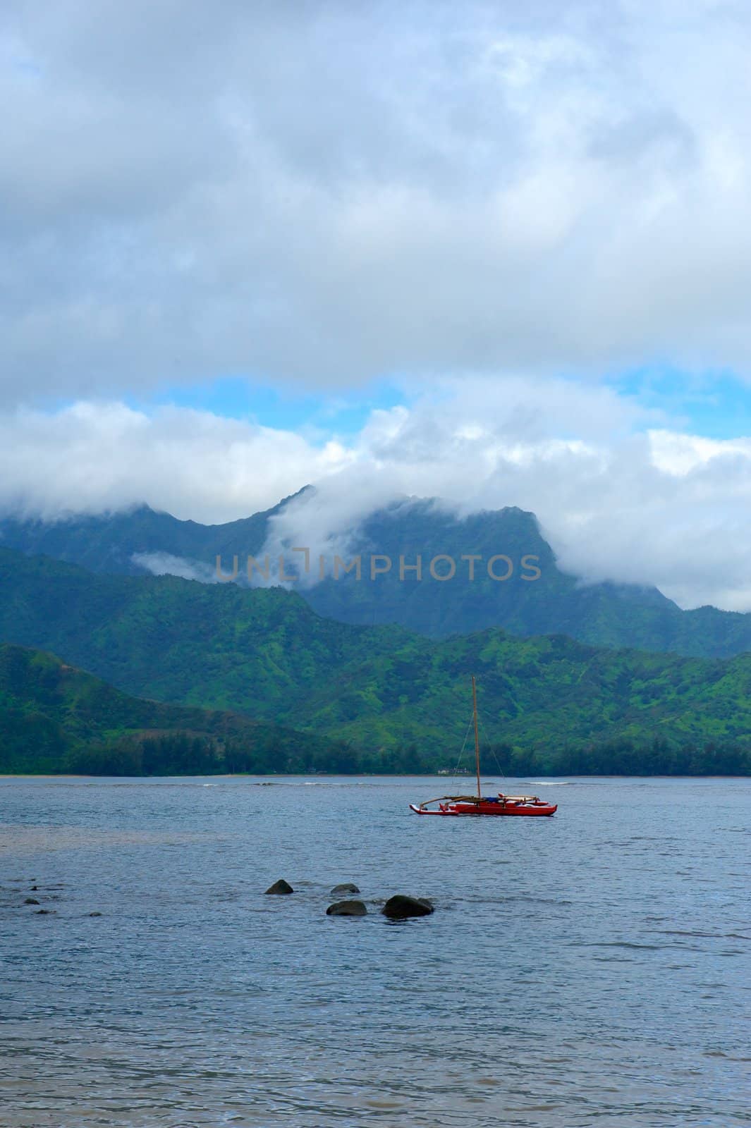 A red, double hull, catamaran sits parked off the verdant green coast of the island of Kauaii in Hawaii