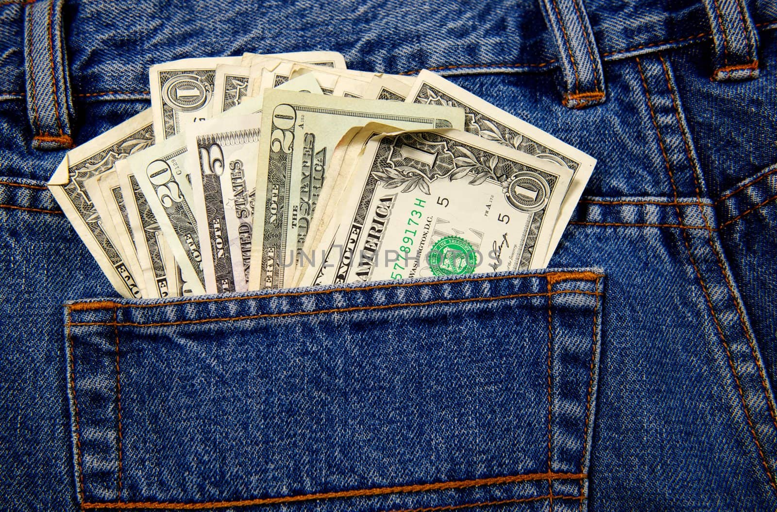 A back pocket of a pair of blue jeans full of currency in US Dollars