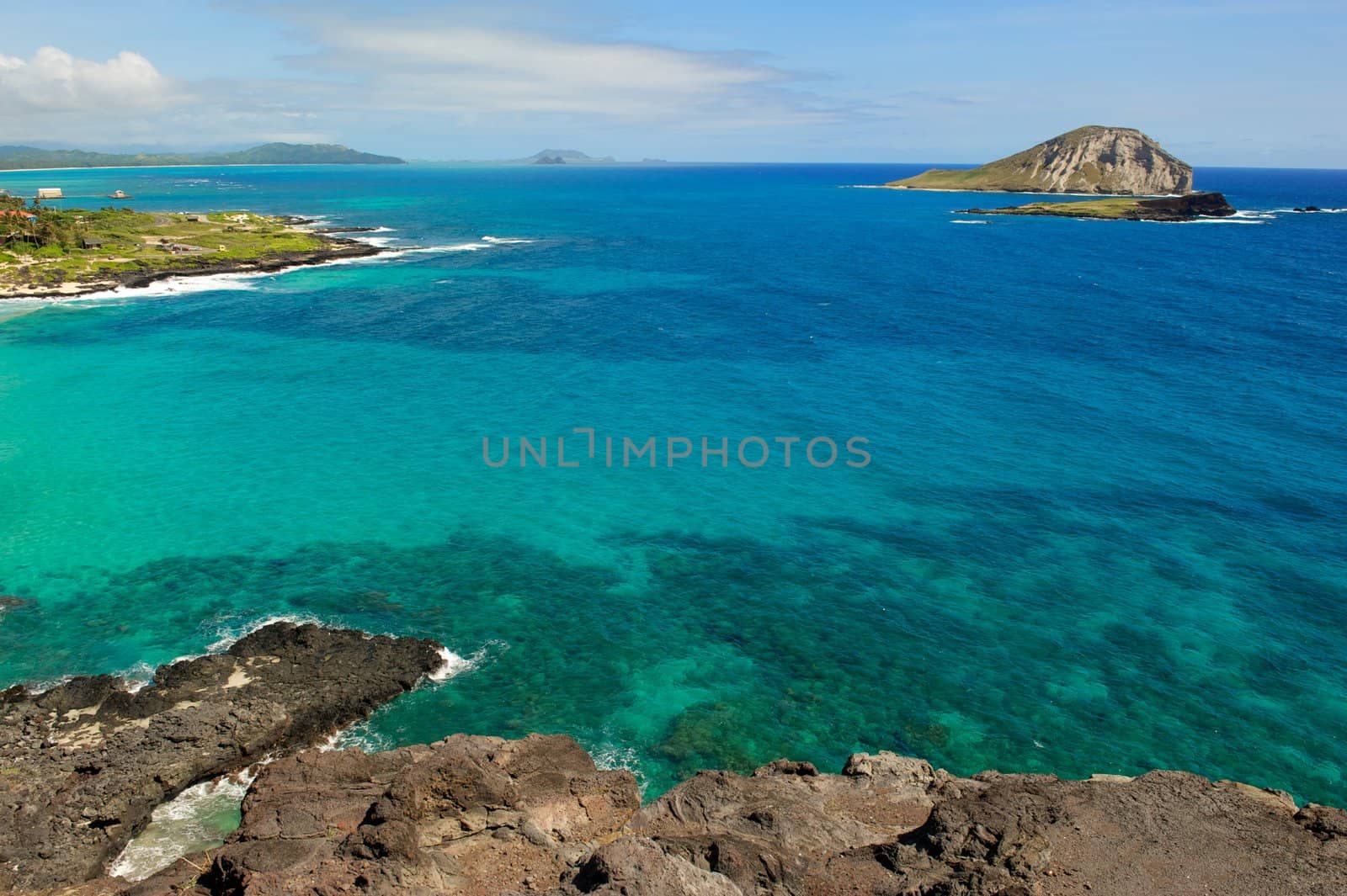 A horizontal shot of the blue and green water off the north coast of the island of Oahu in Hawaii showing several small islands