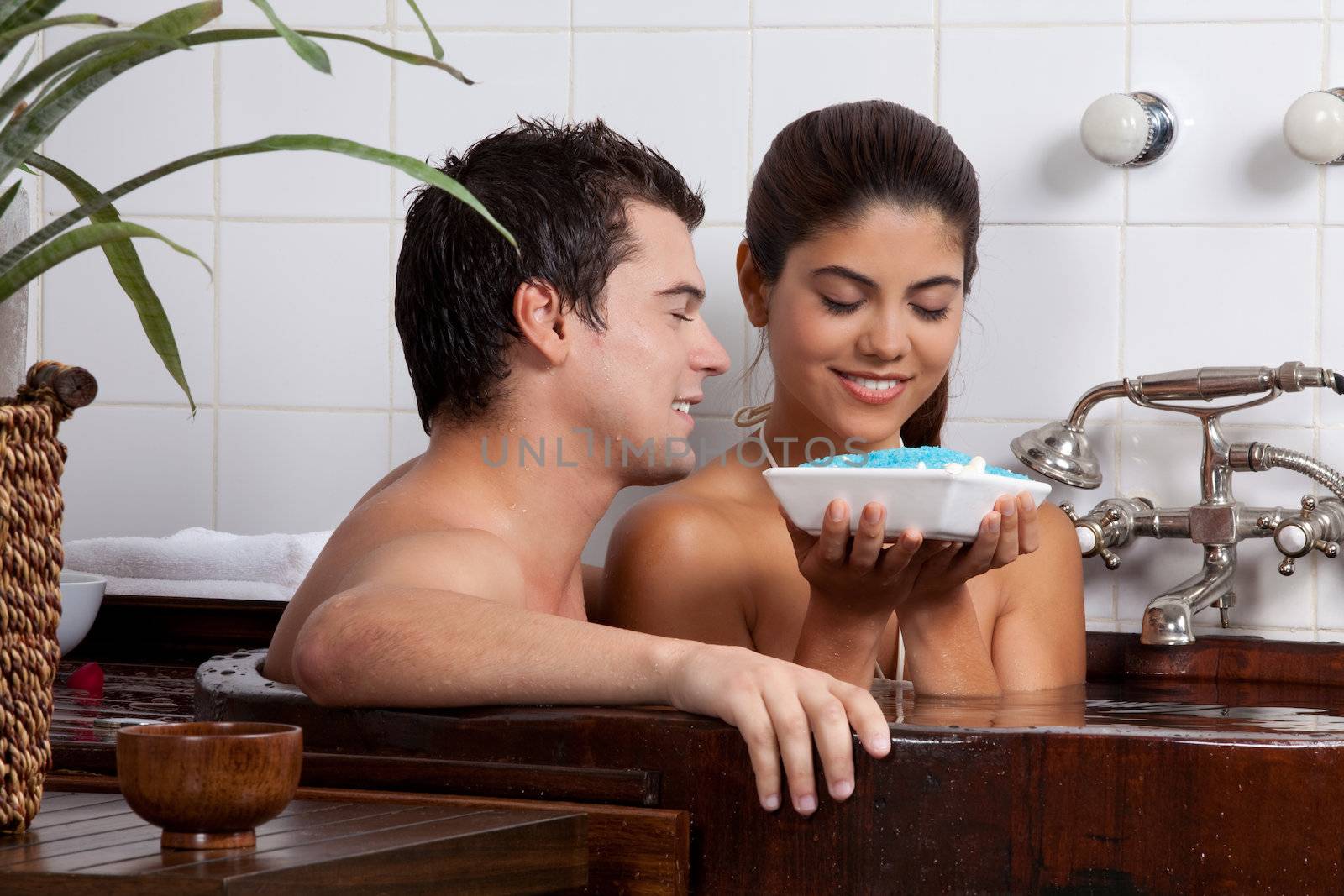 Couple in bath tub holding bath salt in bowl.