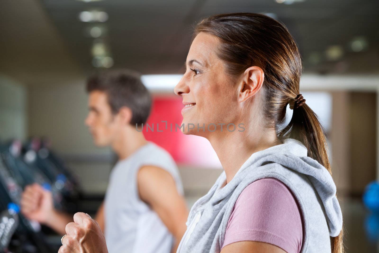 Side view of mature woman and man running on treadmill in health club