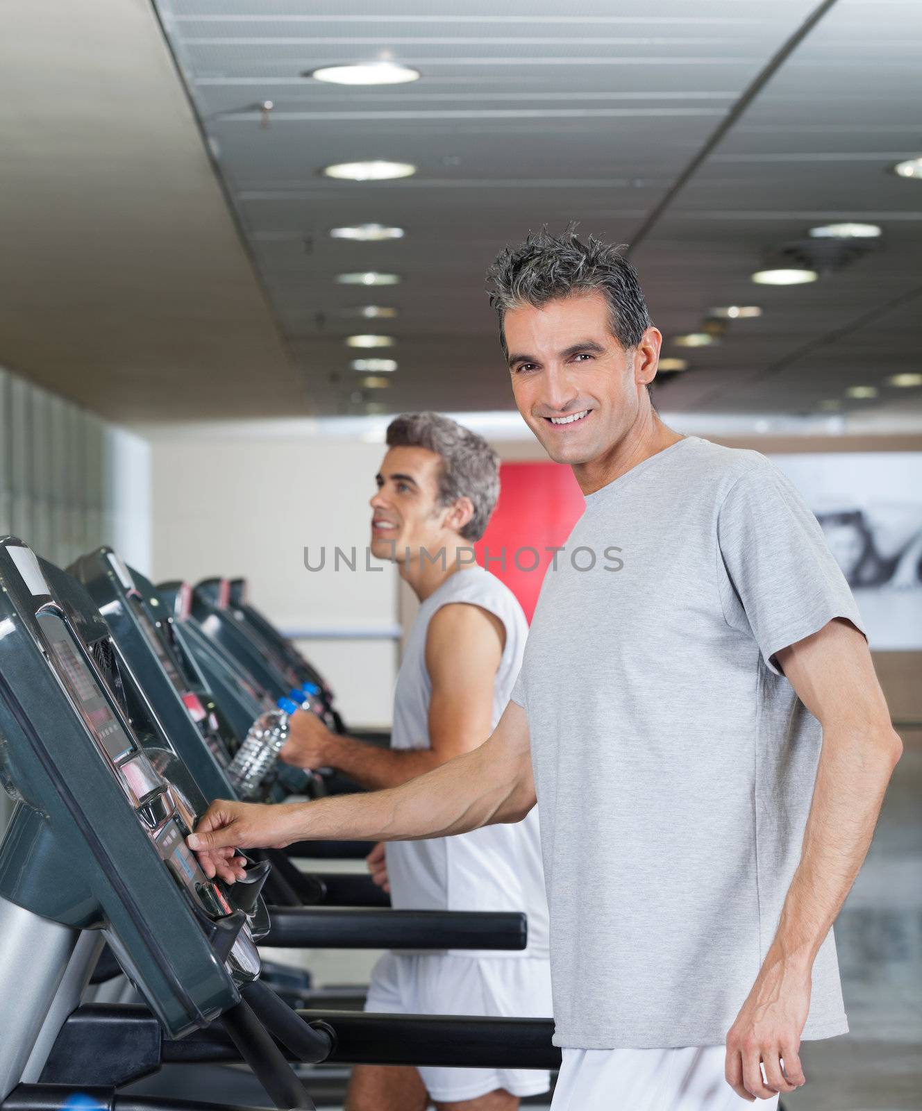 Happy men running on treadmill in fitness center