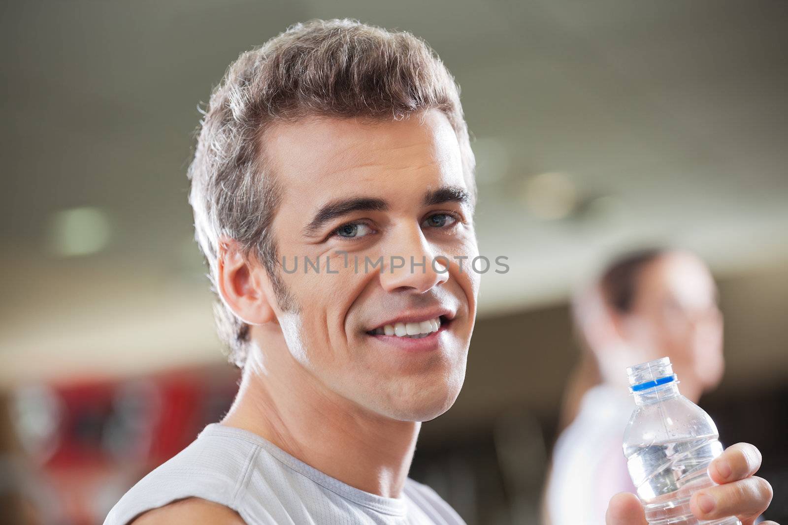 Close-up portrait of young man holding water bottle in health club