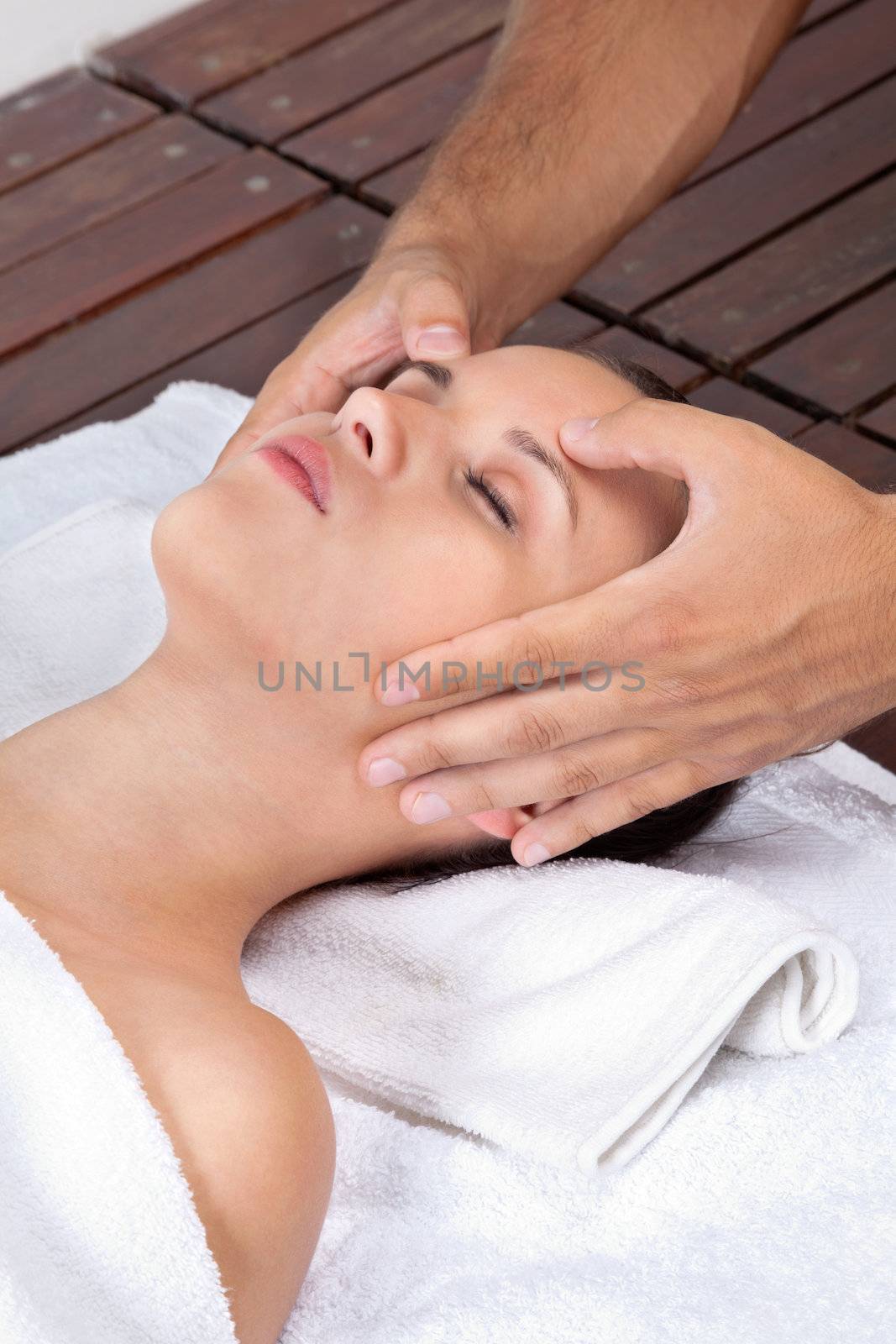 Beautiful young female receiving head massage by a male masseuse at health spa