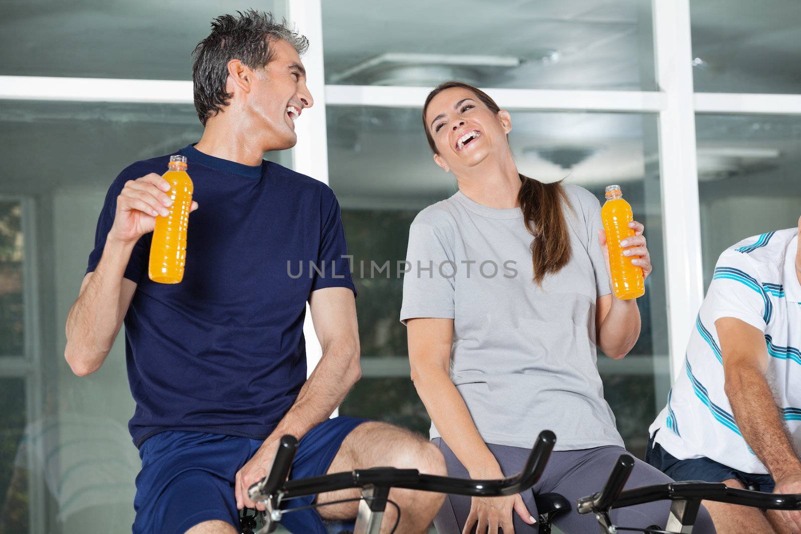 Man and woman holding juice bottles while laughing in health club