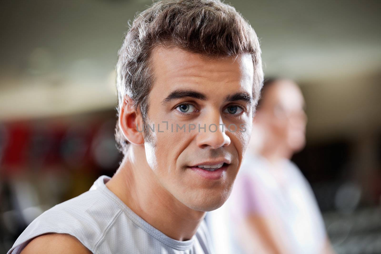 Close-up portrait of young man in health club with woman in the background