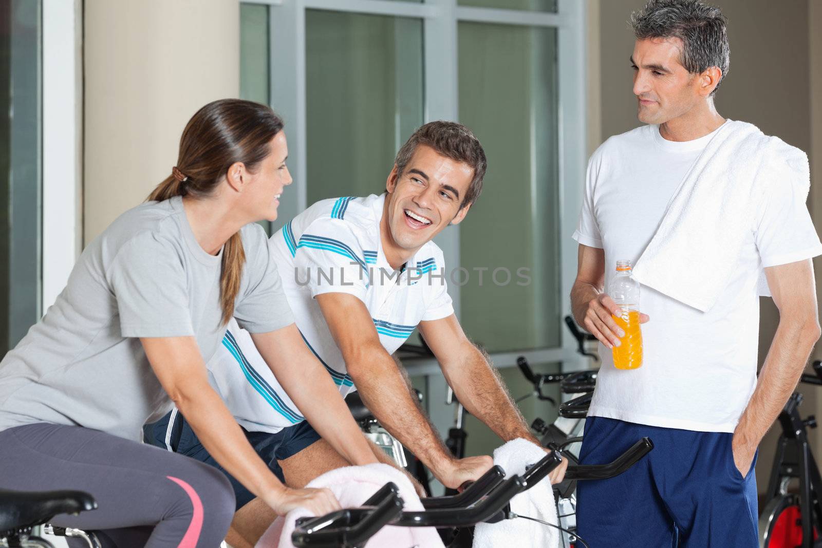 Man looking at happy friends exercising on spinning bike in health club
