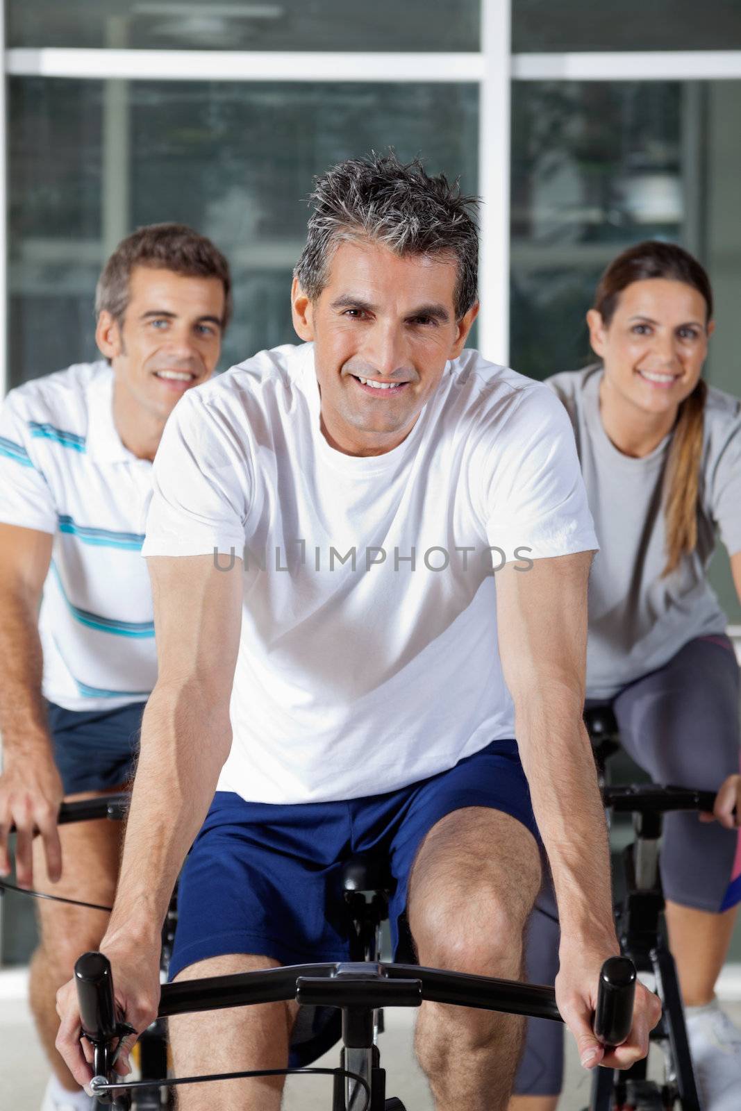 Portrait of three happy people on exercise bikes in health club