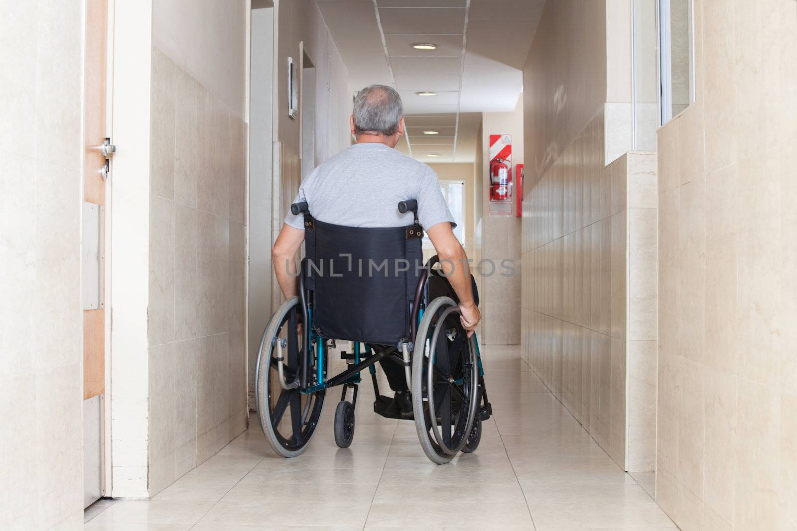Rear view of a senior man sitting in a wheelchair at hospital corridor