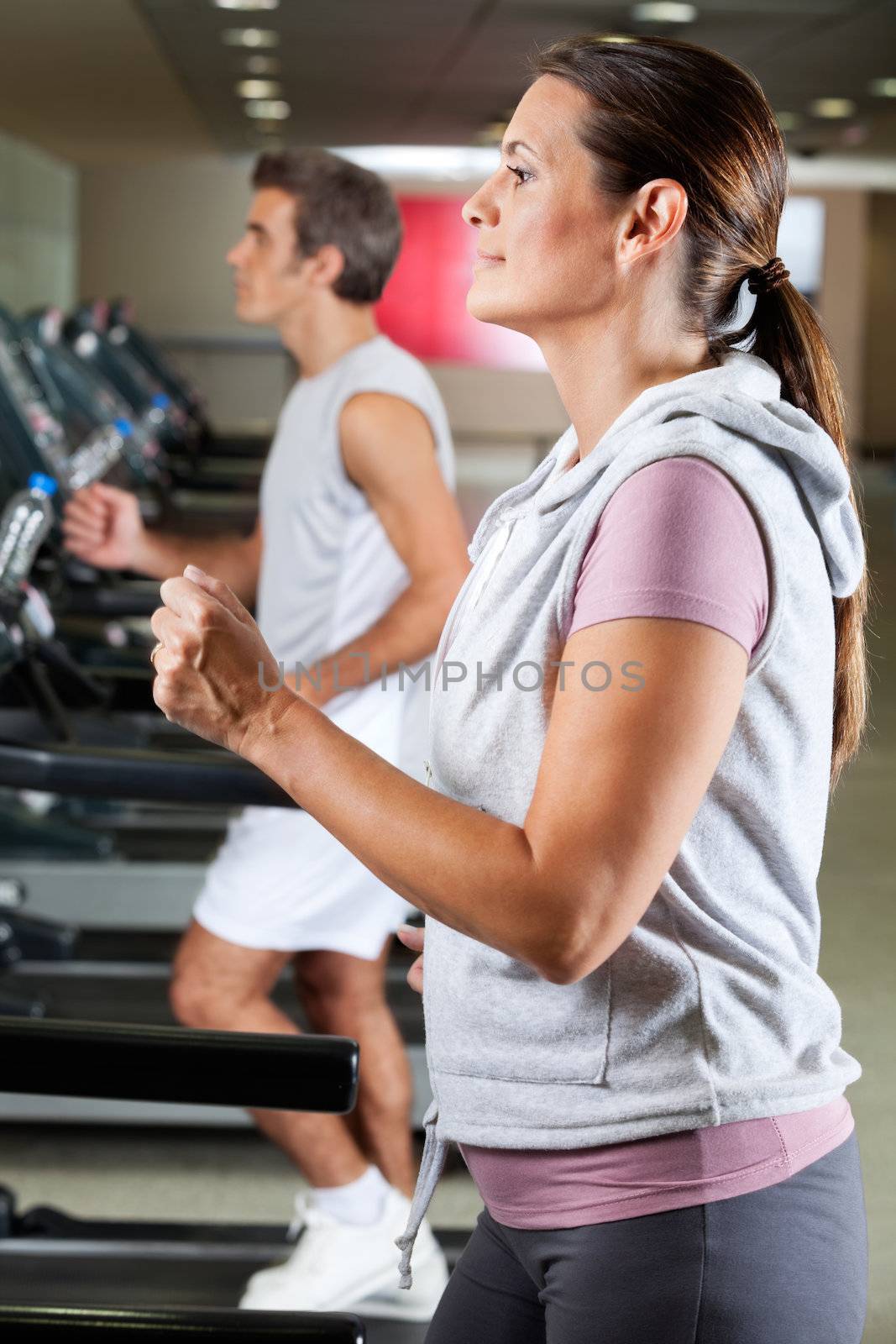 Profile shot of mature woman and man running on treadmill in health club