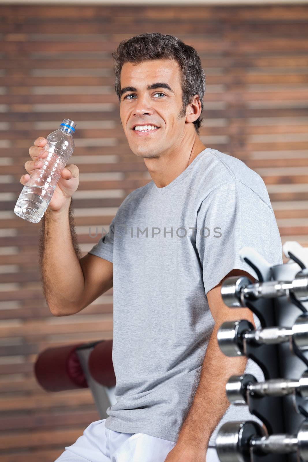 Portrait of happy young man drinking water from bottle at health club