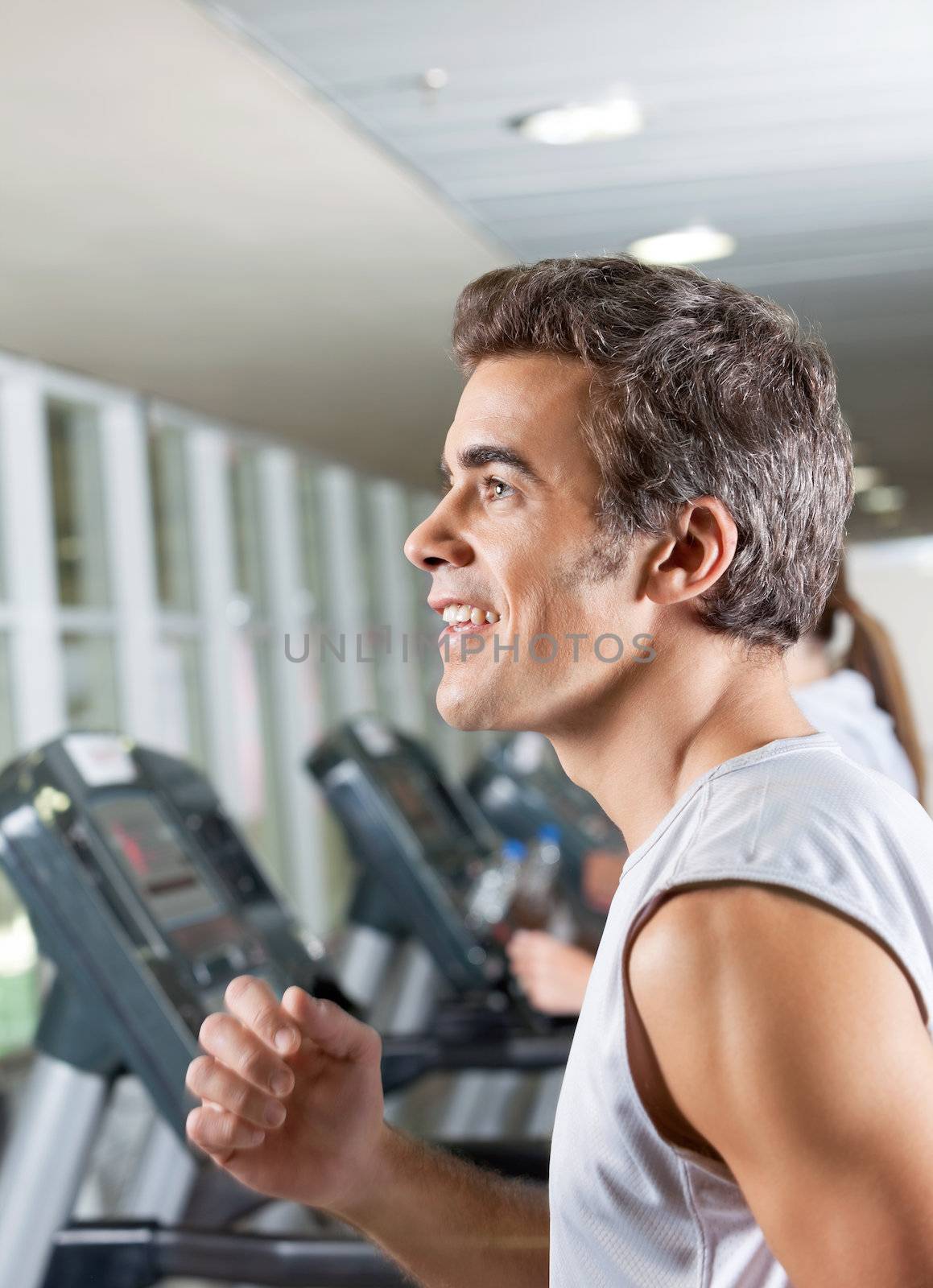 Side view of happy young man and woman running on treadmill in health club