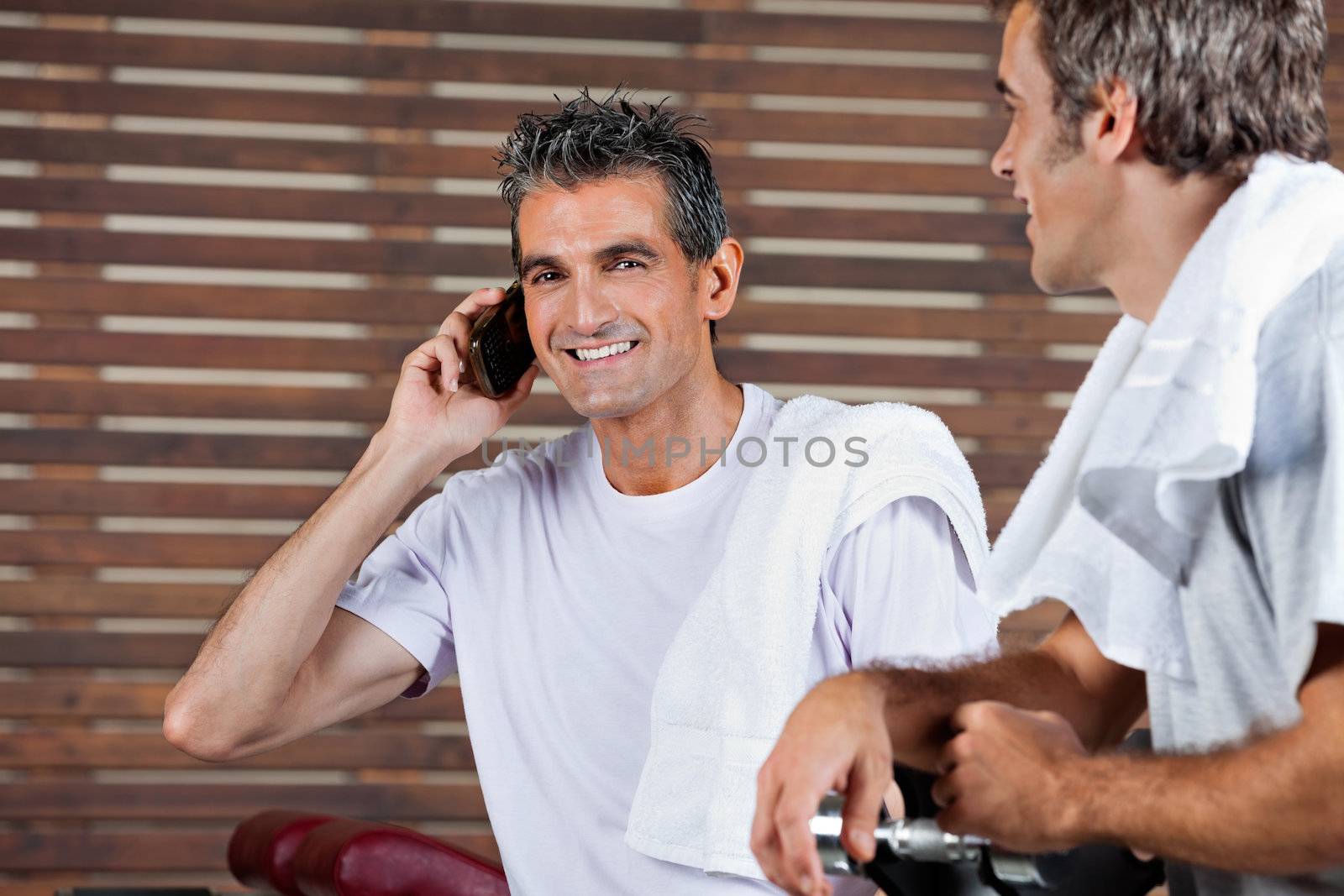 Portrait of happy mature man on call while friend looking at him in health club