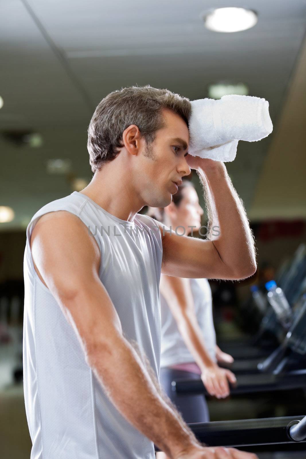 Side view of young man wiping sweat with towel at health club.