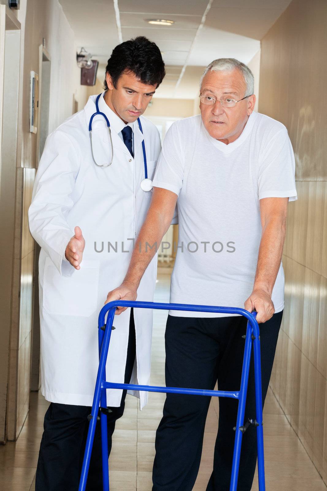 Doctor helping senior patient walk down hallway using Zimmer frame