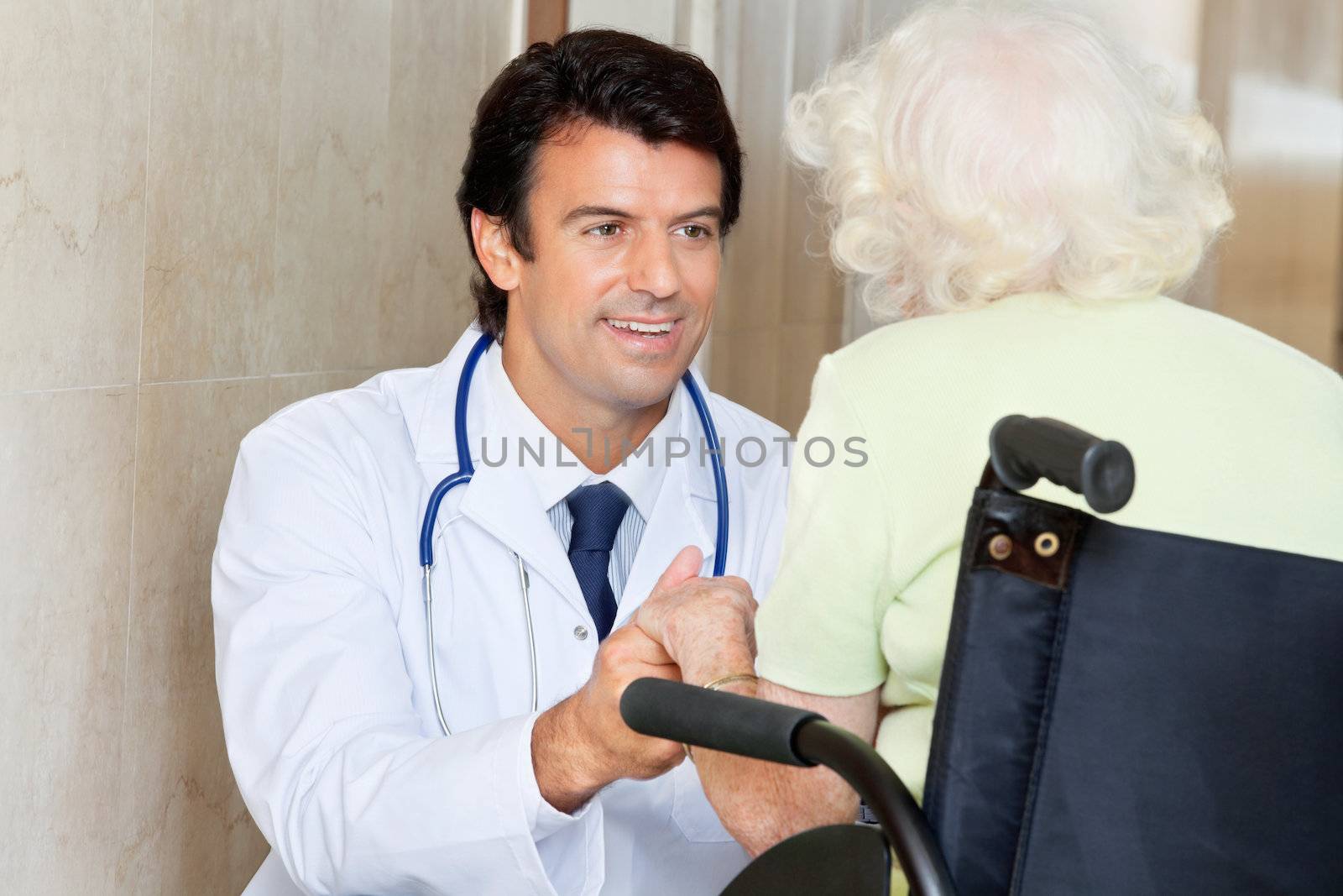 Happy young male doctor looking at senior woman sitting in wheel chair at hospital