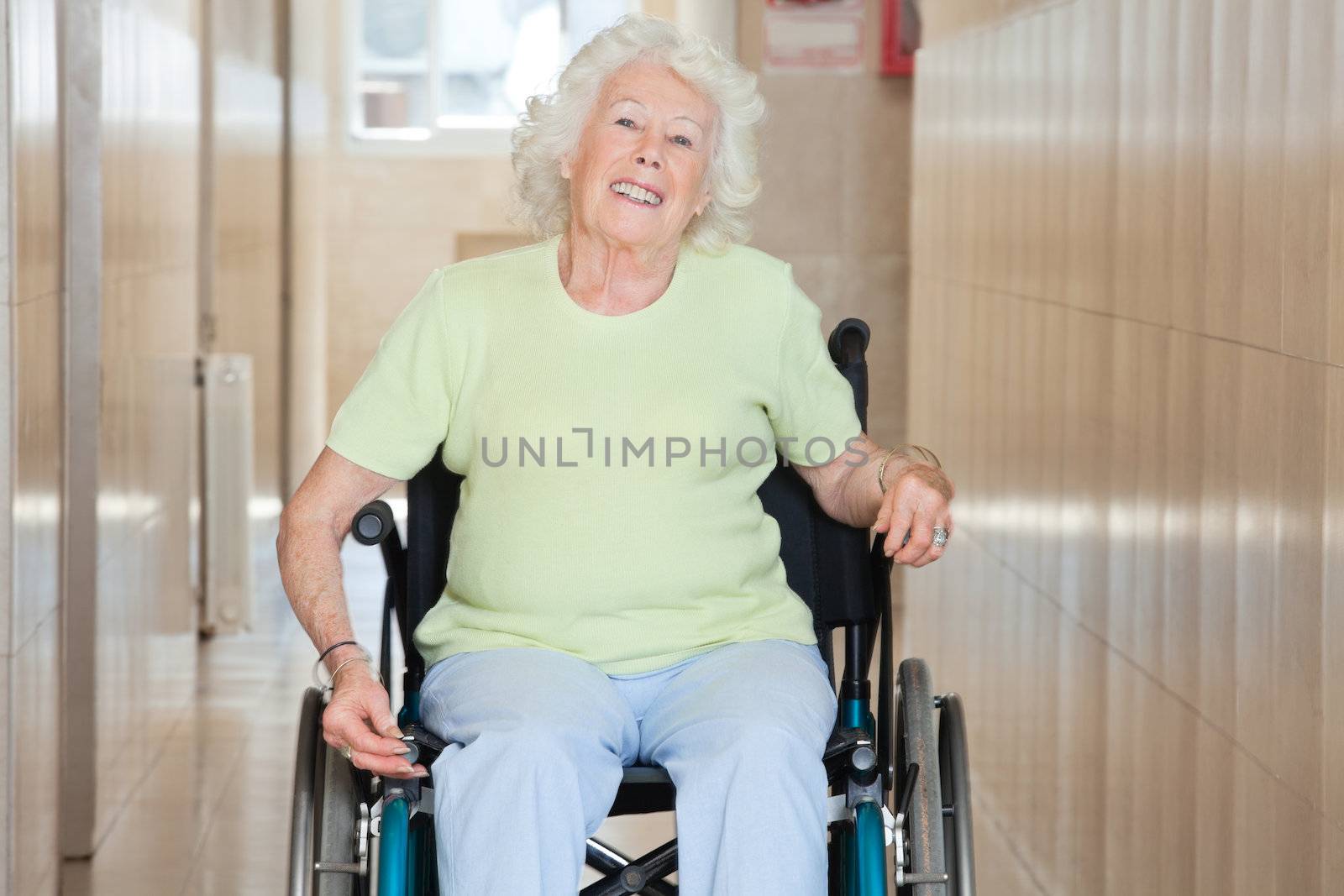 Happy senior woman sitting in a wheel chair at hospital corridor