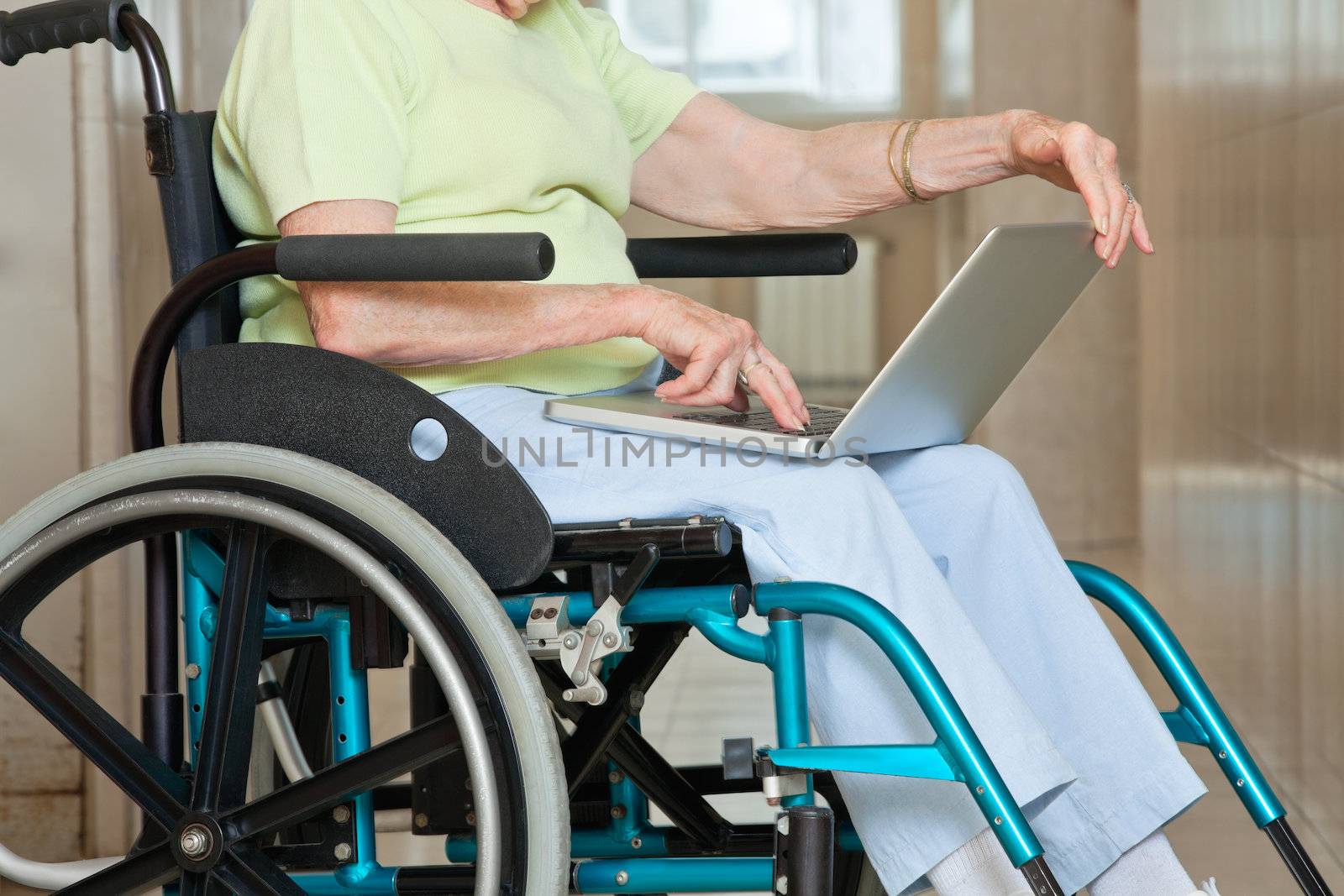 Midsection of senior woman sitting in wheelchair using laptop at hospital