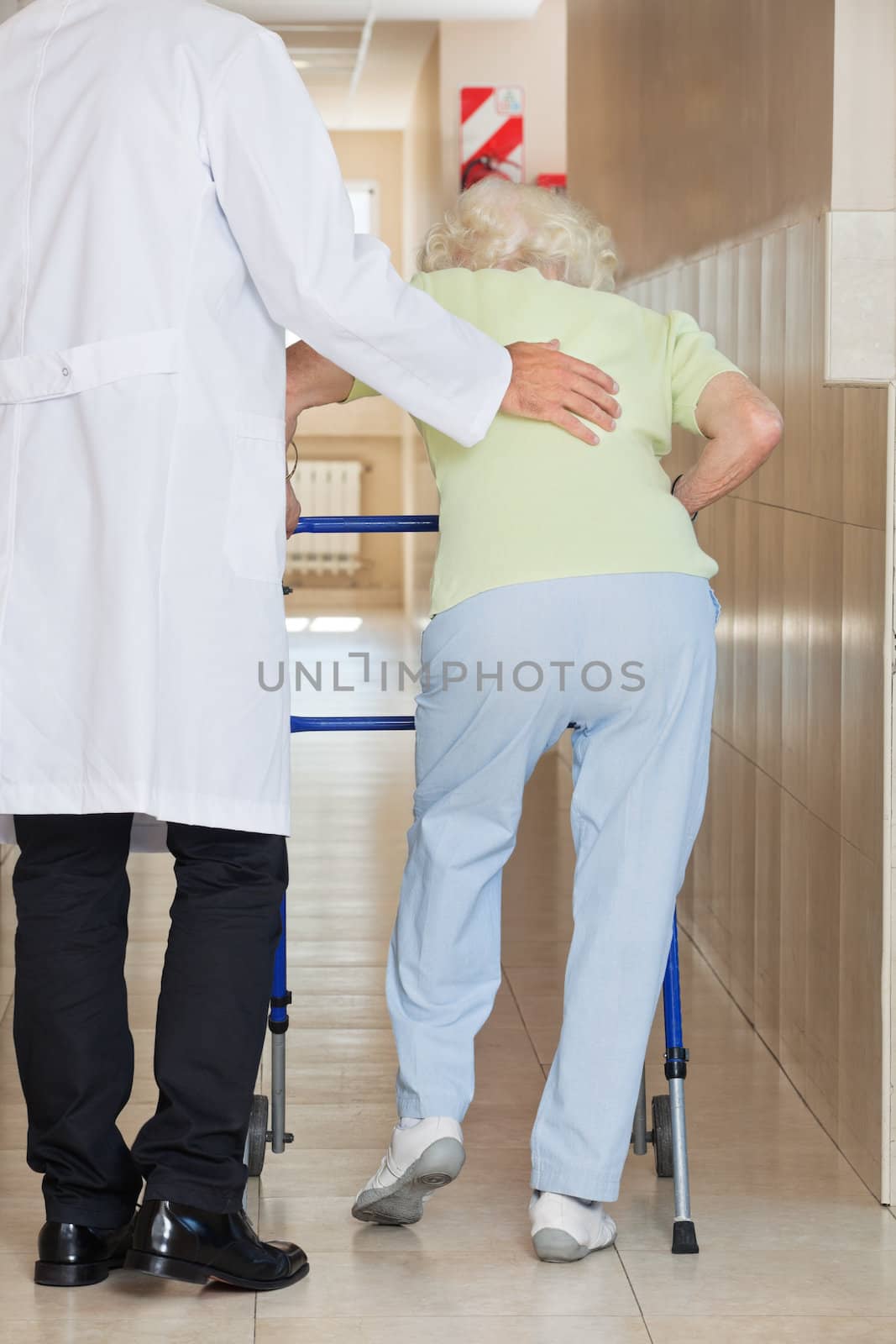 Doctor Assisting Senior Woman To Use Walker by leaf