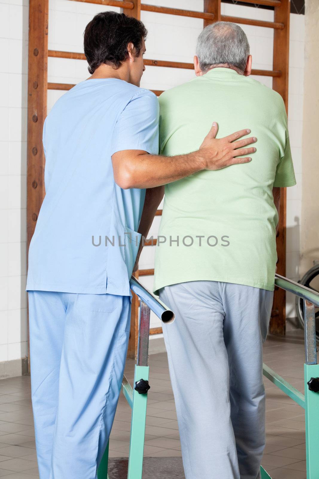 Therapist Assisting Senior Man To Walk With The Support Of Bars by leaf