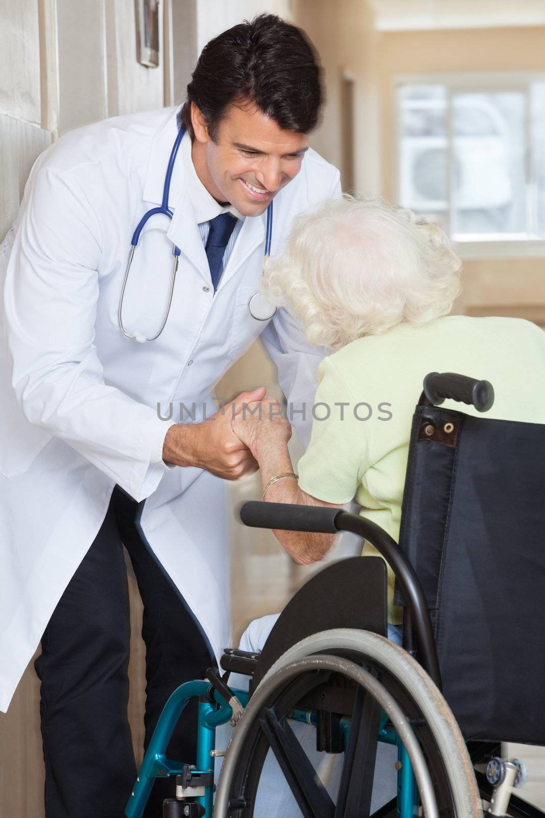 Doctor Assisting Senior Woman In Wheelchair by leaf