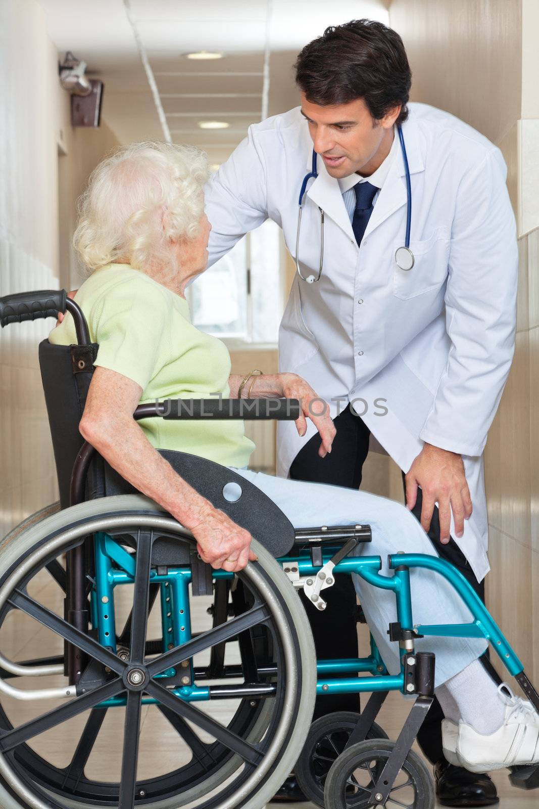 Young doctor communicating with senior female patient sitting in wheelchair at hospital