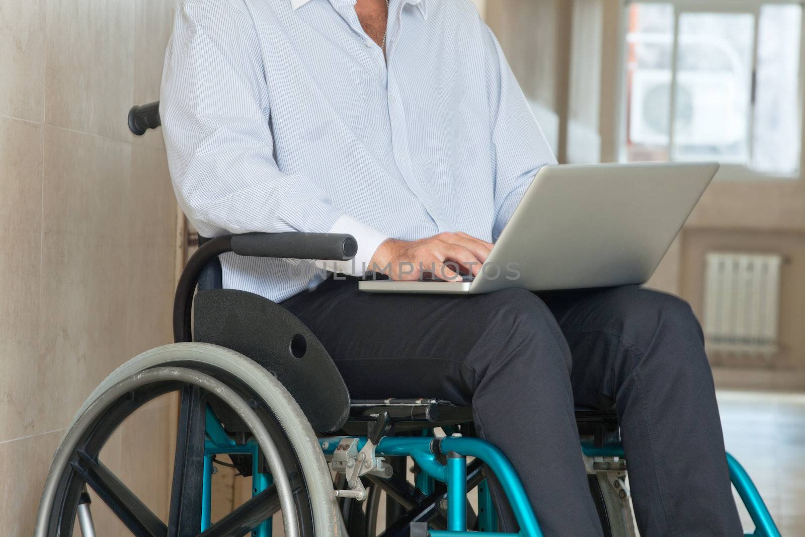Mid section of a man sitting in wheel chair using laptop at hospital