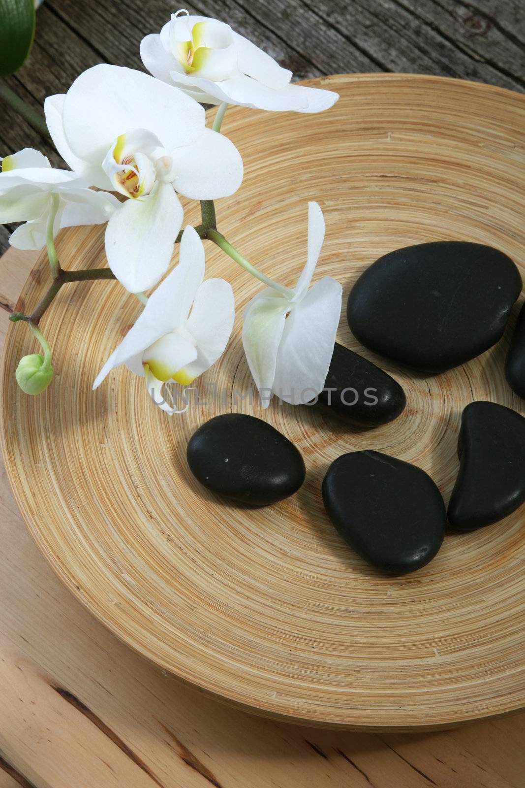 Group of smooth black basalt spa massage stones in a pottery bowl with a spray of fresh white orchids