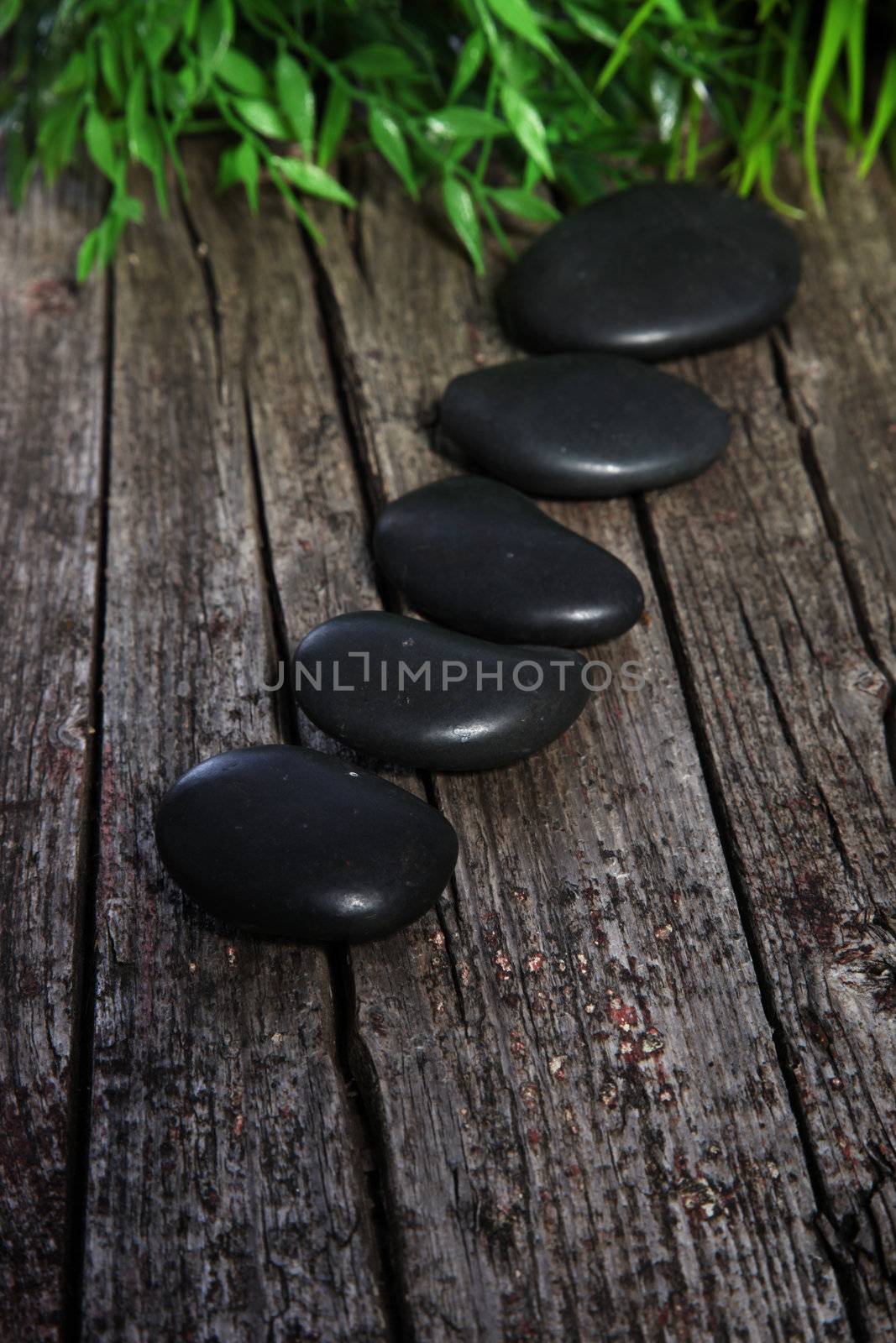 Basalt spa massage stones neatly arranged in a diagonal line on an old wooden surface with green leaves