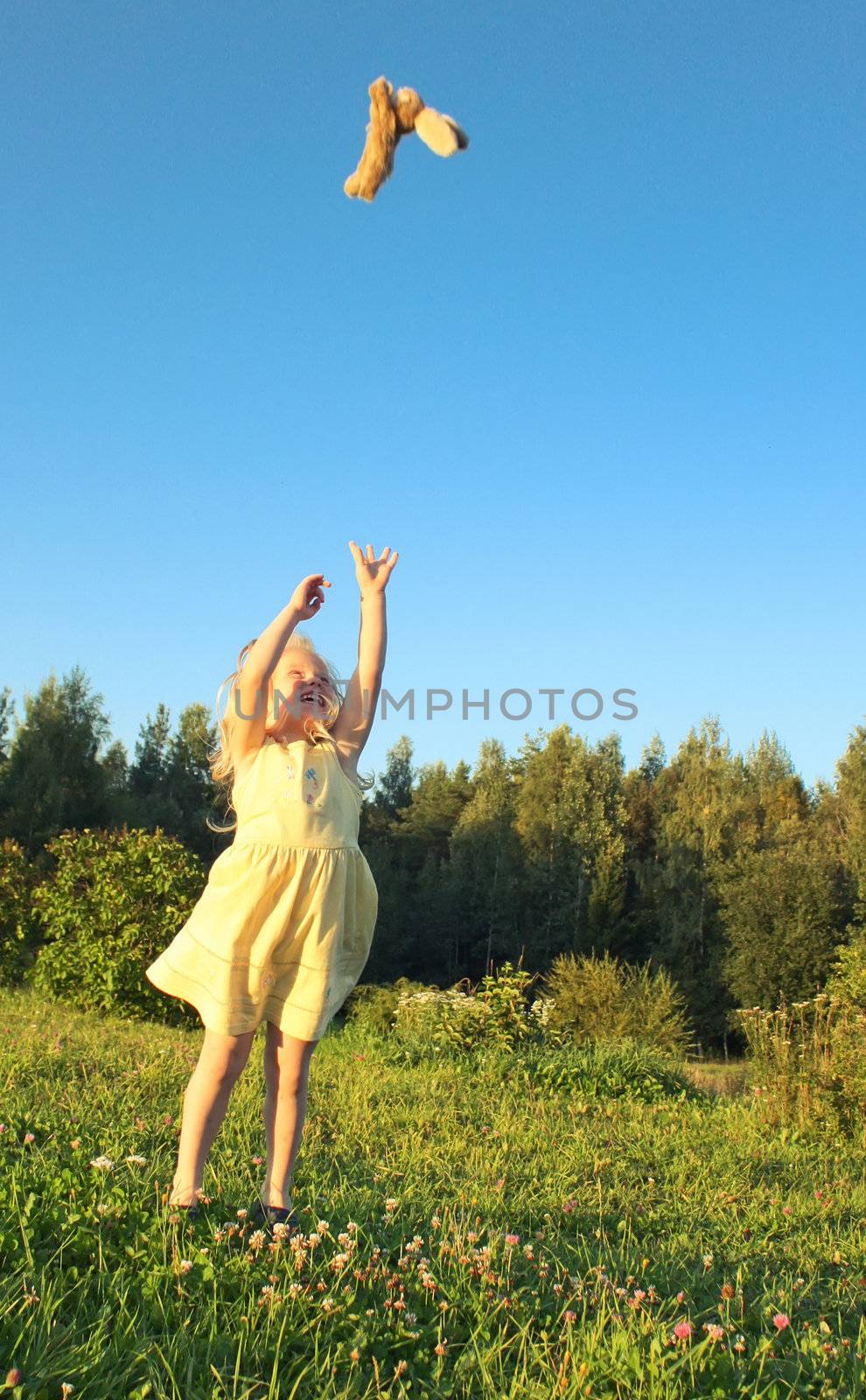 girl in a yellow dress plays with a toy on a background of blue sky