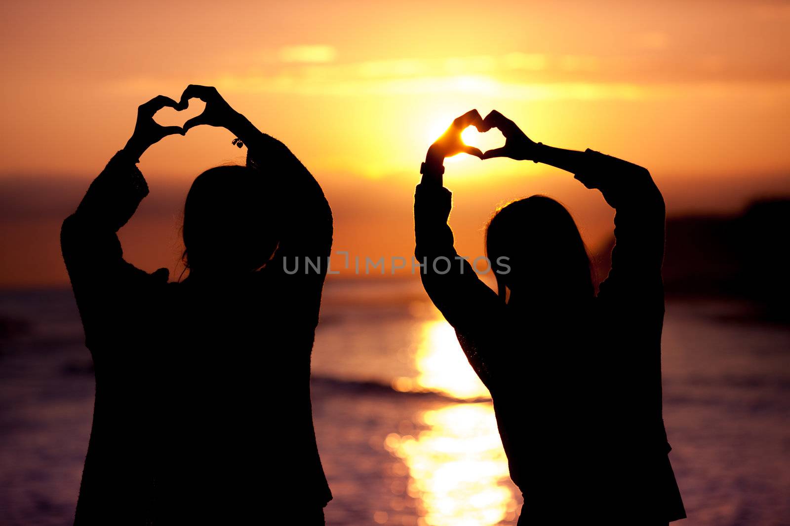 women silhouette makes heart shape sunset